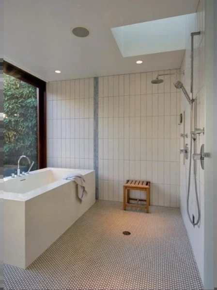 Open wet room with a freestanding tub, teak shower bench, small mosaic floor tile and a skylight