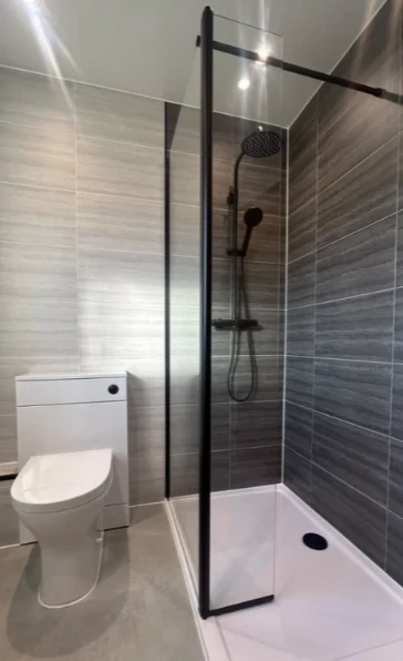 Walk-in shower with black-framed glass screen, gray plank tile and low white shower tray