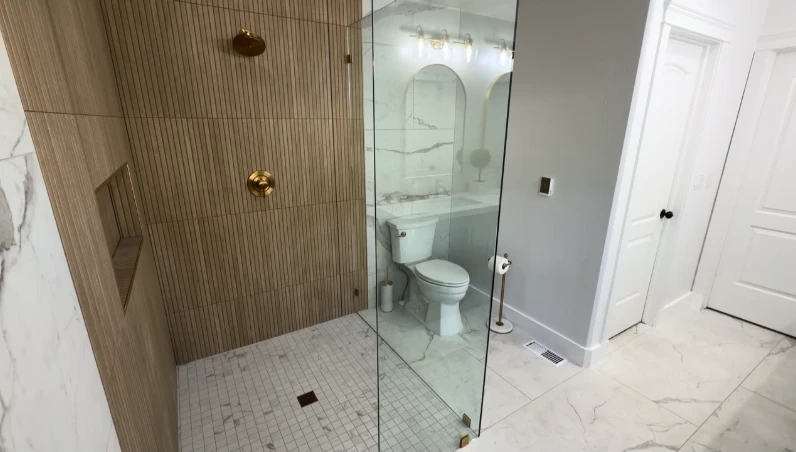 Doorless-style walk-in shower with wood-look tile wall, gold fixtures and a glass panel