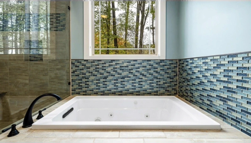 Drop-in whirlpool tub with blue glass tile and a black deck-mounted faucet