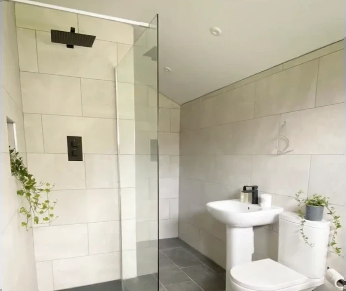 Bright bathroom with a frameless glass walk-in shower, black rain head, large stone-look tile and a pedestal sink