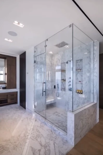 Large glass-walled shower in a marble primary bathroom