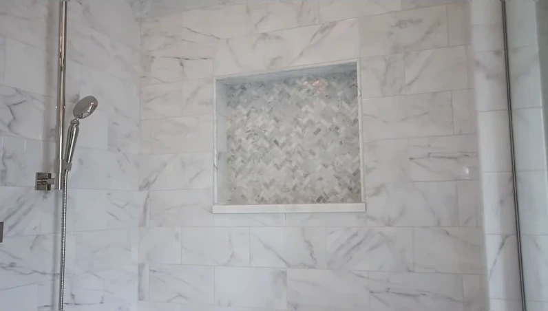 Herringbone mosaic shower niche set into large marble-look wall tile
