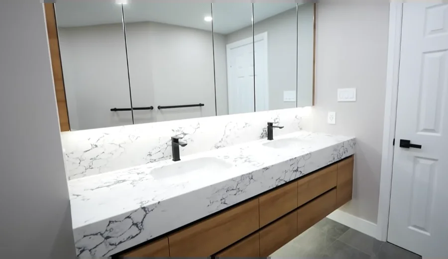 Floating wood double vanity with a marble-look top, two sinks, black faucets and a long mirror cabinet
