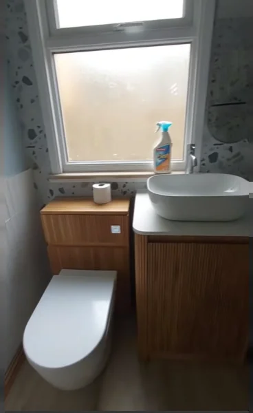 Compact bathroom with a wood vanity, white vessel sink and close-coupled toilet under a frosted window