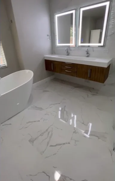 Bright bathroom with glossy marble-look porcelain floor, freestanding tub, floating double vanity and LED mirrors