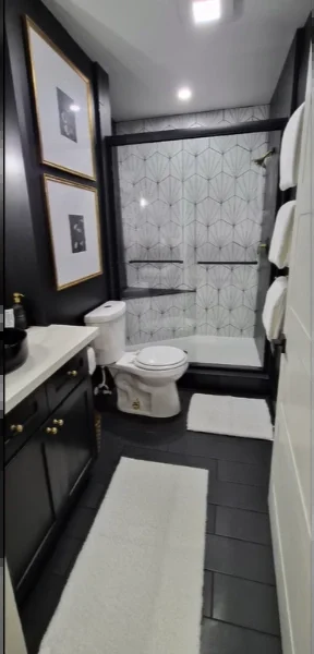 Black and white bathroom with patterned shower tile, black vanity, black floor tile and framed art