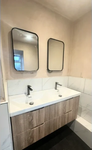 Finished bathroom with a wood-look double vanity, white top, black faucets and two framed mirrors