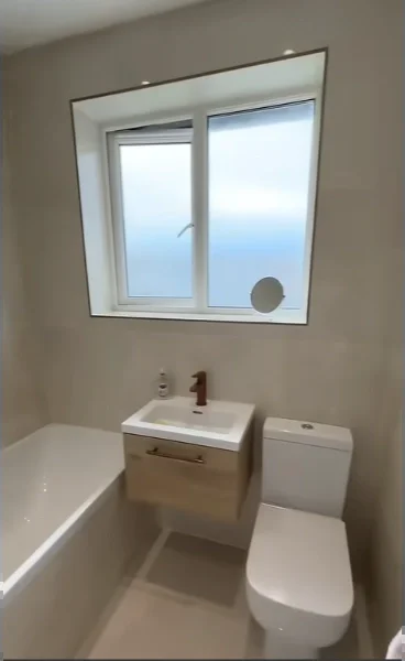 Updated family bathroom with a new tub, small wood vanity, white toilet and neutral tile under the same window