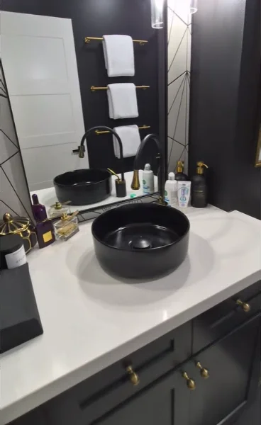 Navy vanity with a white quartz top, black vessel sink, brass towel bar and dark accent wall