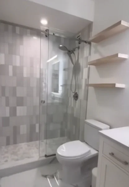 Glass walk-in shower with stacked gray tile, a lit mirror niche and floating wood shelves