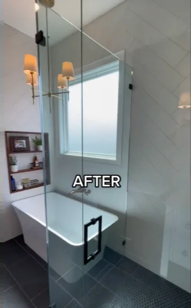 Freestanding tub inside a glass wet room enclosure with gray tile, sconces and a built-in shelf