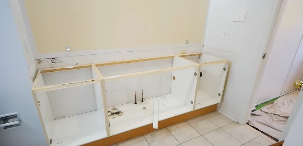 Old bathroom vanity stripped down to its frame during demolition, with plumbing exposed