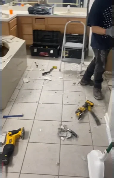 Bathroom floor tile being removed during demolition, with tools and debris on the floor
