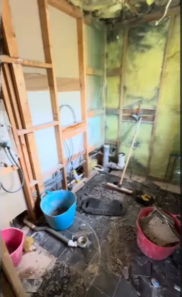 Bathroom opened to the studs with exposed plumbing, old wallboard and buckets on the floor
