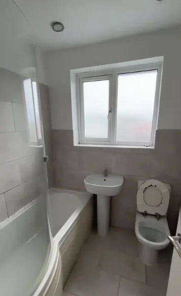 Older bathroom with a curved tub, pedestal sink, toilet and dated wall tile under a window