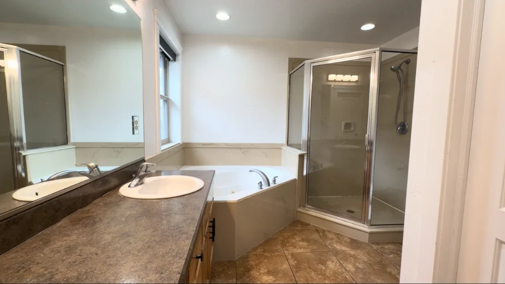 Dated primary bathroom with a corner tub, neo-angle glass shower and brown laminate double vanity