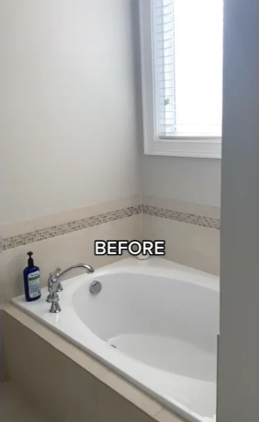 Old drop-in bathtub with a tile border and a single faucet under a window