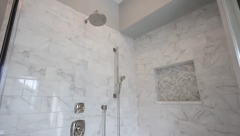 Rain shower head and handheld sprayer on a slide bar beside a tiled niche