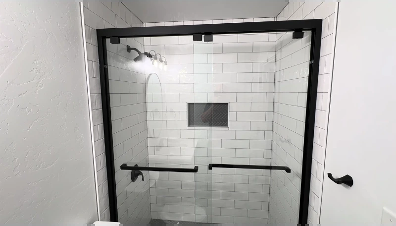 Walk-in shower with white subway tile, black framed sliding glass and a recessed niche