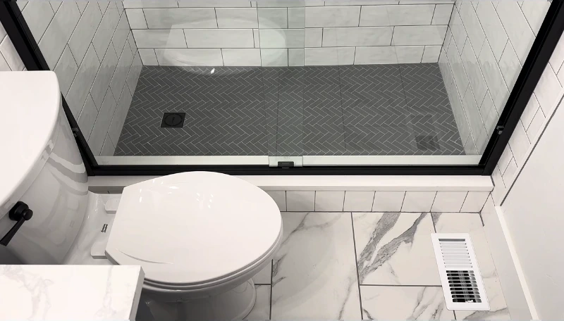 Shower with a dark herringbone tile floor, white subway walls and marble-look bathroom floor
