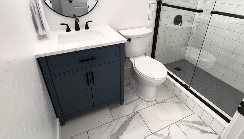 Navy vanity with white top, black hardware, toilet and glass shower in a finished small bathroom