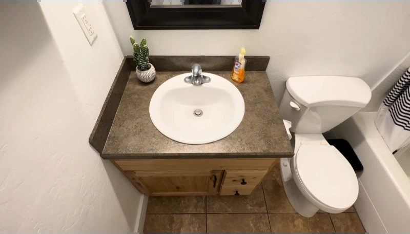 Outdated vanity with a laminate top and round sink beside a toilet before the remodel