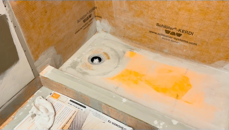 Shower pan covered with orange waterproofing membrane and a center drain during construction