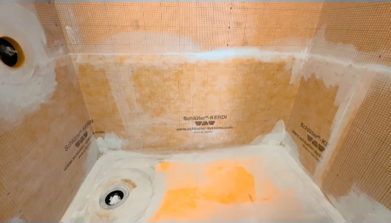 Shower walls and floor lined with orange waterproofing membrane during the remodel
