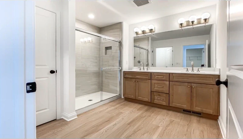 Remodeled bathroom with a wood double vanity, sliding glass shower with tile surround and wood-look flooring