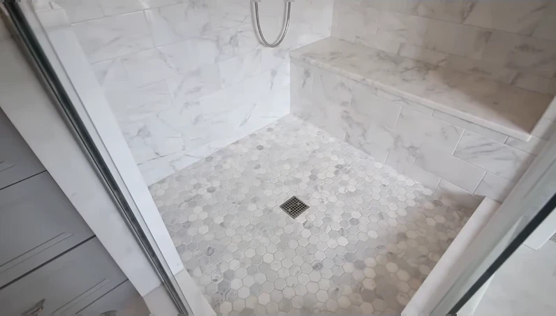 Inside a tiled shower: built-in bench and hexagon mosaic floor with a center drain