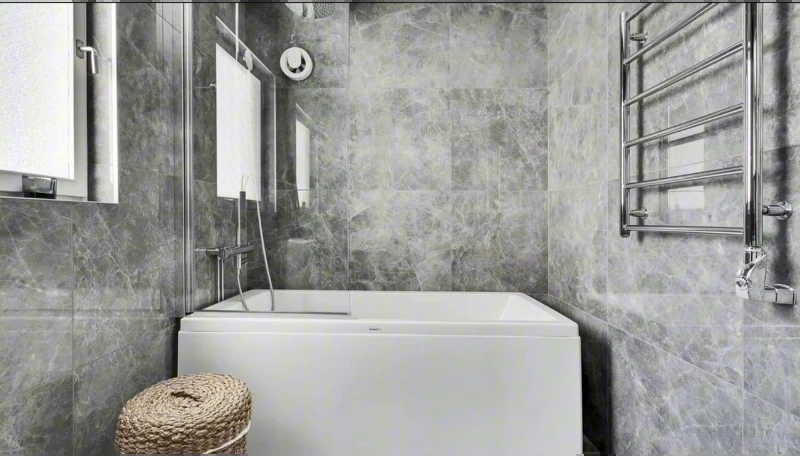 Compact white alcove tub with gray tile walls and a heated towel rail