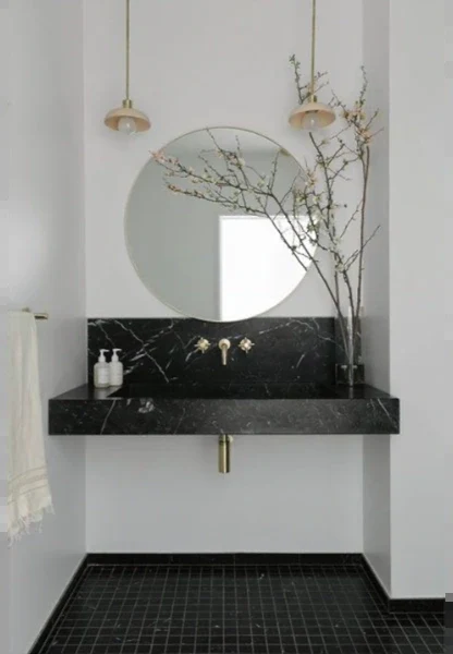 Wall-hung black marble sink with open space underneath, a brass wall-mounted faucet and a round mirror