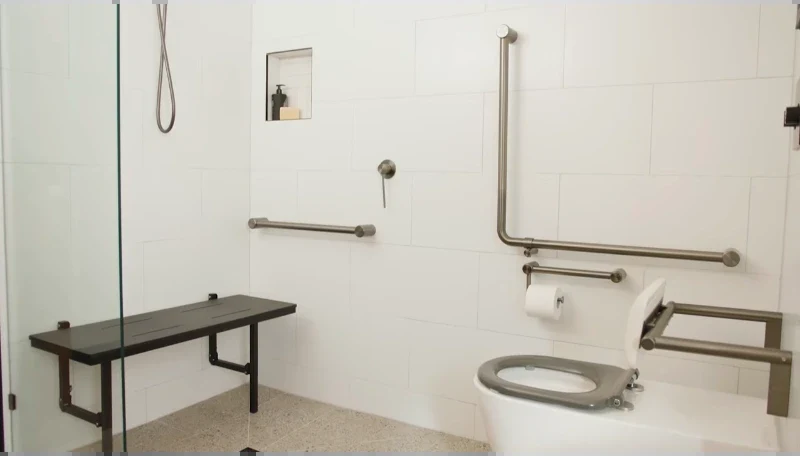 Wall-mounted folding shower bench next to a tiled niche, lever shower valve and horizontal and L-shaped grab bars